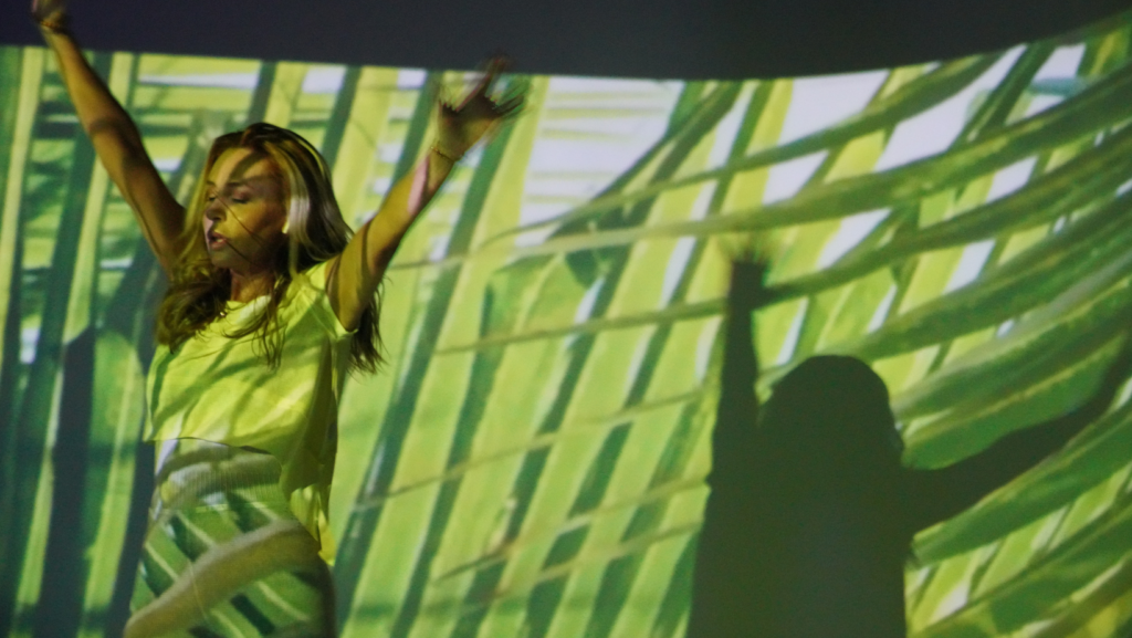 Person energetically dancing in front of a vibrant green and yellow abstract background, symbolizing rejuvenation and recovery from burnout