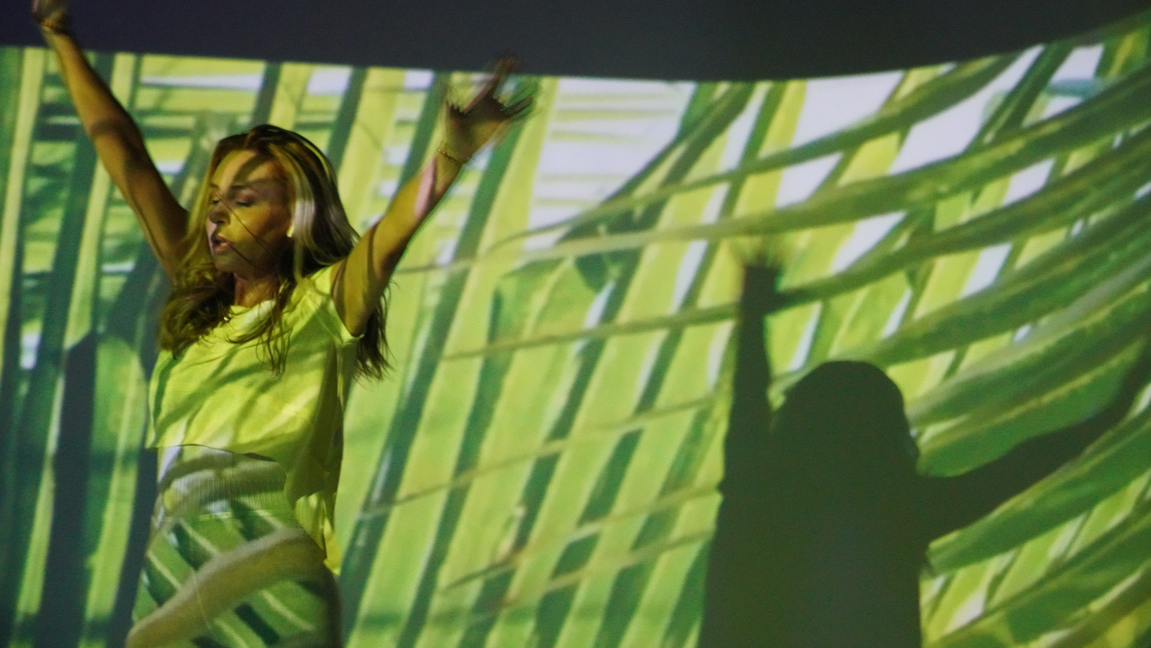 Person energetically dancing in front of a vibrant green and yellow abstract background, symbolizing rejuvenation and recovery from burnout